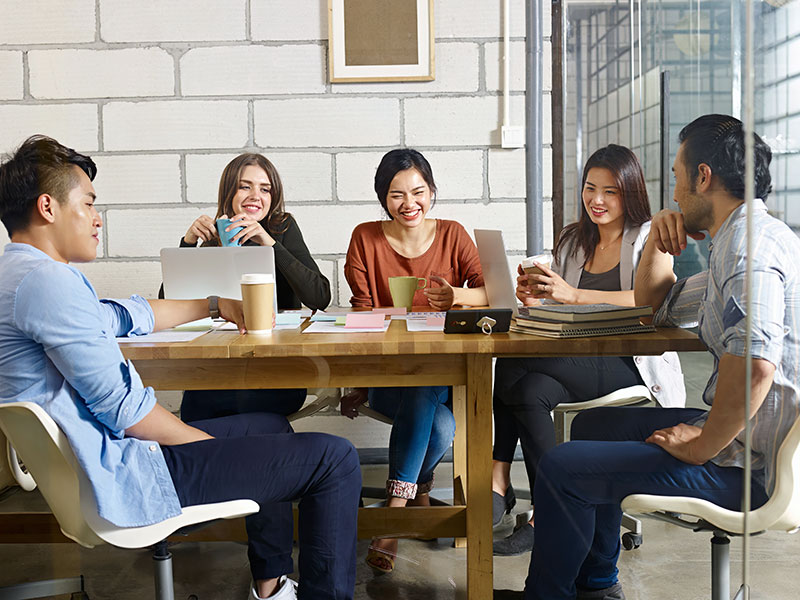 Five adults meeting around a table smiling and laughing
